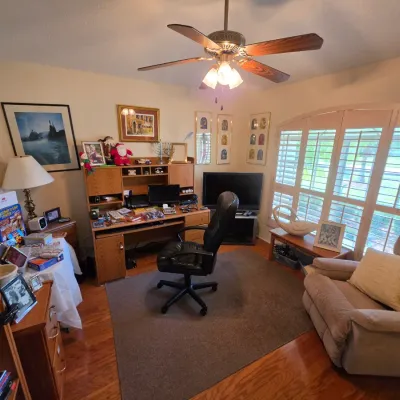 Home office furniture set including a wooden desk with hutch, a black leather rolling office chair, a plush beige recliner, and various...