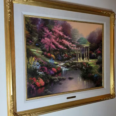 Thomas Kinkade framed canvas print depicting a lush garden landscape with a stream and gazebo, housed in an ornate gold-finished frame...