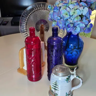 Assorted decorative glassware including a red and a purple embossed bottle, a cobalt blue vase with faux hydrangeas, a cut glass platter,...