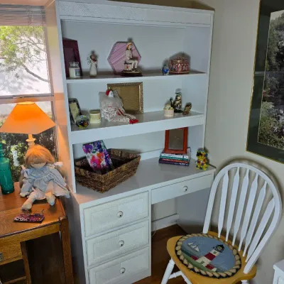 White wooden desk with an integrated hutch, featuring textured drawer fronts, paired with a white Windsor-style chair with a...