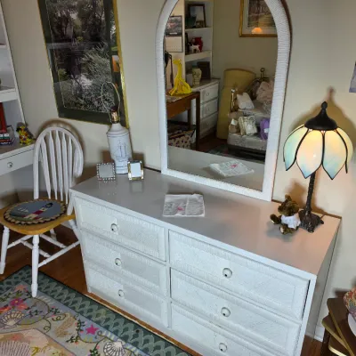 White wicker six-drawer dresser with matching arched mirror, accompanied by a white wooden Windsor-style chair with a lighthouse seat...