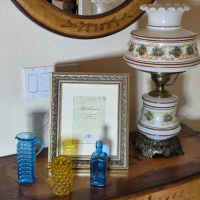 Vintage hurricane-style table lamp with floral milk glass shade and base, displayed alongside an ornate gold picture frame and small...