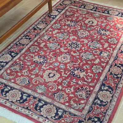 Traditional Persian-style area rug featuring an intricate floral pattern in red, navy blue, and cream tones with fringed edges.