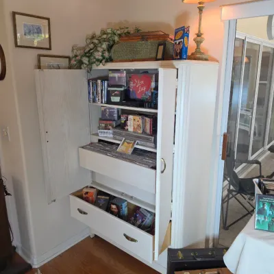 White wooden media armoire with pull-out drawers and shelves, filled with various DVDs, CDs, and media storage.