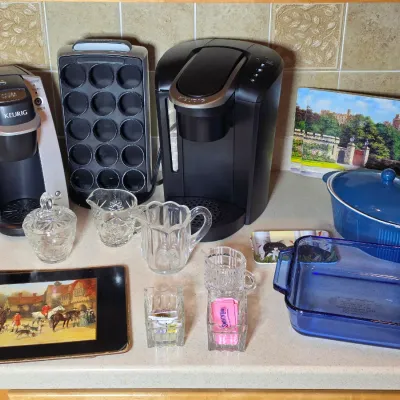 Assorted kitchenware including two Keurig coffee makers, a K-cup holder, cut glass creamers and sugar bowls, blue Pyrex baking dishes,...