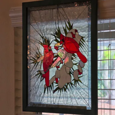 Stained glass window panel depicting two red cardinals perched on snow-covered pine branches, set in a dark wooden frame.