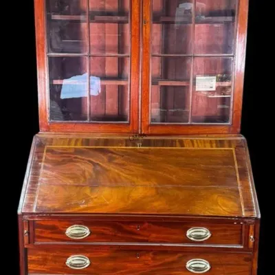 Antique mahogany secretary desk featuring a glass-door bookcase top, a slant-front writing desk, and four lower drawers with brass hardware.