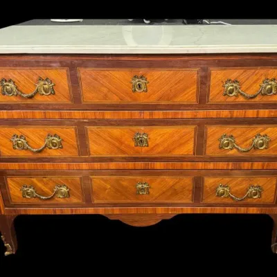 French Louis XV style commode featuring a white marble top, parquetry inlaid wood drawers, and ornate brass hardware.