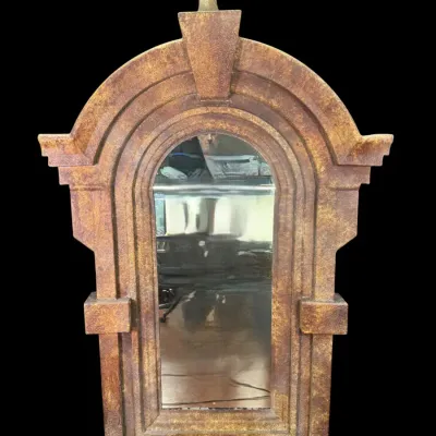 Arched wall mirror featuring a textured, rust-toned frame with architectural details and a ball finial.
