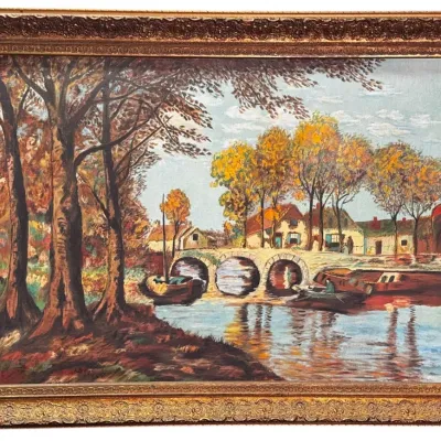 Impressionistic oil landscape painting depicting a river scene with a stone bridge, boats, and autumn trees, housed in an ornate gilded...