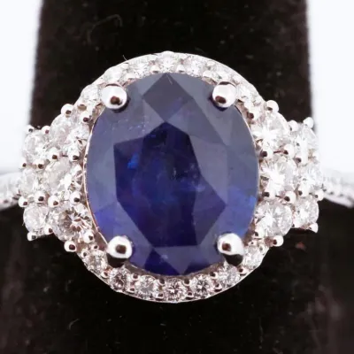 Elegant white gold or platinum ring featuring a large, oval-cut blue sapphire center stone surrounded by a halo of small diamonds and...