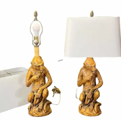 Pair of vintage Hollywood Regency style monkey table lamps with a textured gold finish, pineapple finials, and white rectangular fabric...