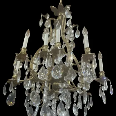 Vintage brass and crystal chandelier featuring six candle-style lights, ornate scrollwork arms, and numerous faceted teardrop prisms.