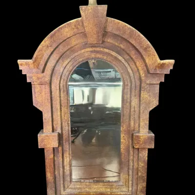 Large architectural wall mirror featuring a textured, rust-toned faux stone frame with an arched top, keystone detail, and a ball finial.