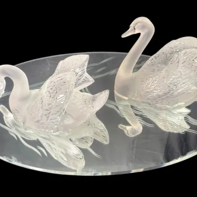 Lalique frosted and clear crystal swan figurines, presented on a mirrored oval plateau with etched water ripple details.