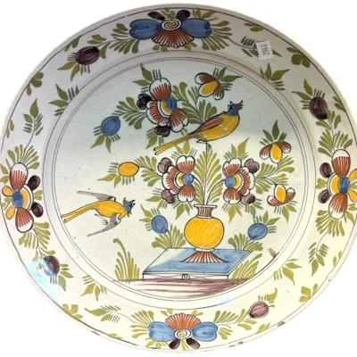 Hand-painted ceramic charger plate featuring a folk art design of birds and flowers in a vase, showing some age-related crazing.