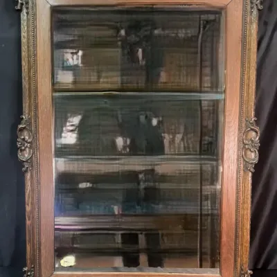 Antique oak wall-mounted display cabinet featuring an ornate carved wood frame with scrollwork details and glass shelves.