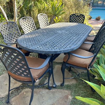 Cast aluminum outdoor dining set featuring an oval lattice-pattern table and matching armchairs with brown cushions.