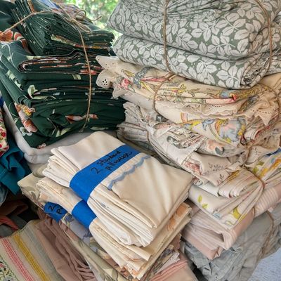 Assorted vintage bed linens and fabric bundles, featuring floral and patterned sheets and pillowcases tied with twine.