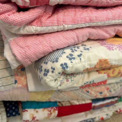 Stack of vintage handmade quilts featuring various patterns including pink gingham, floral prints, and colorful patchwork designs.