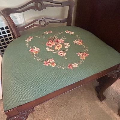 Vintage vanity chair featuring a dark wood frame with carved cabriole legs and a green needlepoint seat cushion adorned with a floral...