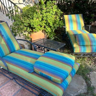 Pair of vintage wrought iron chaise lounges with colorful striped cushions and matching headrest pillows, accompanied by a small black...