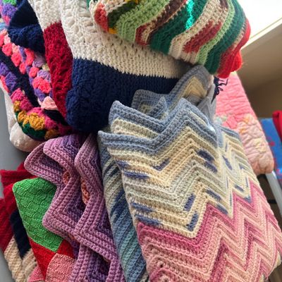 A collection of vintage handmade crochet blankets and afghans in various colorful patterns, including chevron and granny square designs.