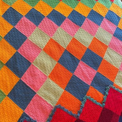 Handmade knit patchwork blanket featuring a vibrant checkerboard pattern in shades of orange, pink, blue, green, and red with a ruffled...