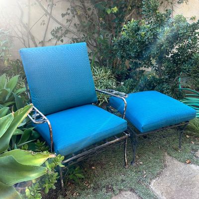 Vintage wrought iron patio armchair and matching ottoman, featuring scrollwork details and bright turquoise cushions.