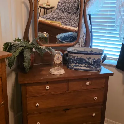 Antique wooden dresser with an attached swivel mirror, featuring white ceramic knobs, styled with a glass dome clock and a blue and white...