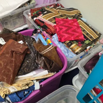 Assorted fabric scraps and quilting quarters in various colors and patterns, organized in plastic storage bins.