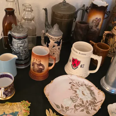 Assortment of vintage collectibles including German beer steins, a Colorado Academy 1967 mug, a floral porcelain plate, and decorative...