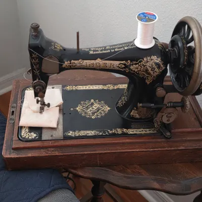 Vintage Singer sewing machine with ornate gold decals, manufactured in Great Britain, mounted on a wooden base.