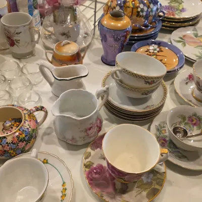 Assortment of vintage porcelain teacups, saucers, creamers, and small plates featuring various floral and hand-painted designs.