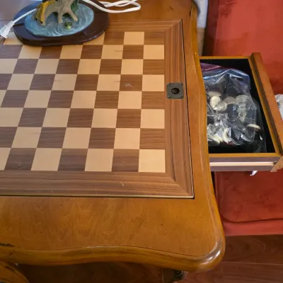 Vintage wooden game table featuring an inlaid chessboard top and a pull-out drawer containing a bagged set of chess pieces.