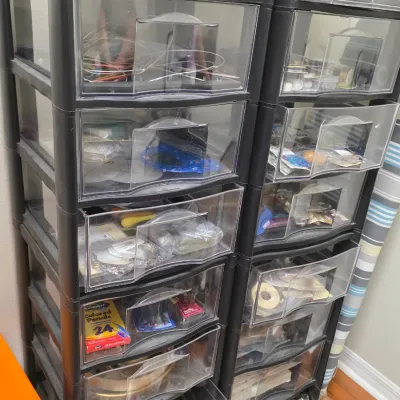 Two black plastic rolling storage carts with clear drawers, filled with various craft supplies, colored pencils, and small tools.