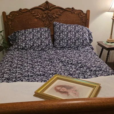 Antique carved oak bed frame featuring an ornate floral headboard, shown with blue and white floral bedding and a framed vintage portrait...