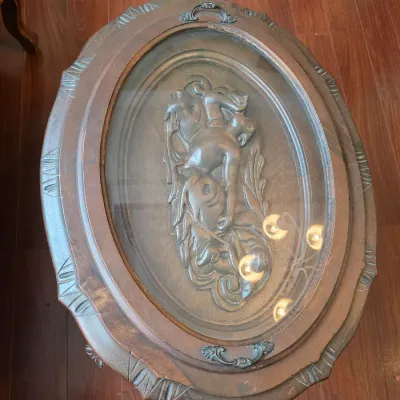 Vintage oval wooden coffee table featuring a glass top insert that reveals a carved relief depicting a figure and a horse.
