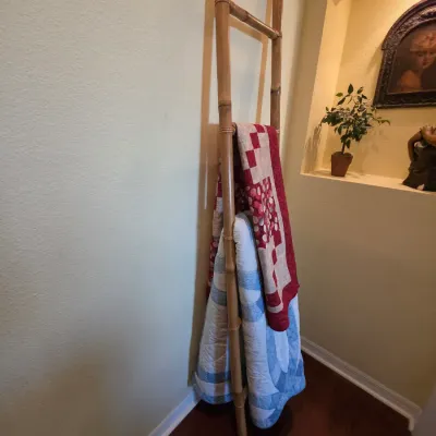 Decorative bamboo blanket ladder leaning against a wall, displaying a red and white patterned quilt and a blue and white quilt.