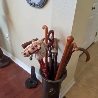 Collection of vintage walking canes, walking sticks, and a child's toy stick horse displayed in a cylindrical metal umbrella stand.