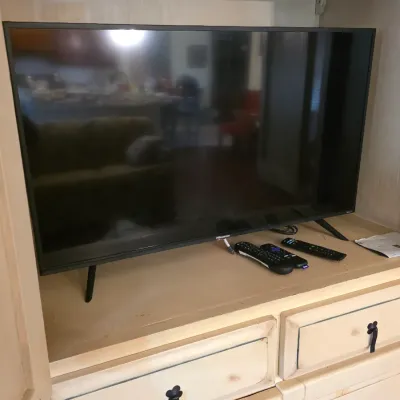 Hisense flat-screen television with three remote controls, displayed on a wooden entertainment center.