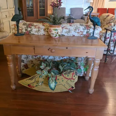 Light pine sofa table with a single drawer and turned legs, styled with decorative crane statues, a floral planter, and a vintage-style...