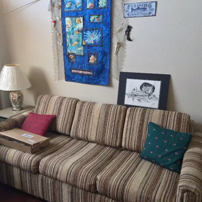 Vintage three-cushion sofa with brown and beige striped upholstery, shown with a blue ocean-themed wall hanging and fishing decor.