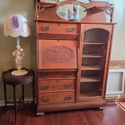 Antique oak side-by-side secretary desk and bookcase cabinet featuring a drop-front writing surface, carved details, and an oval mirror...