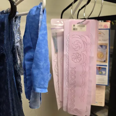 Assorted quilting supplies, including blue fabric scraps and pink plastic border stencils hanging on a closet rod.