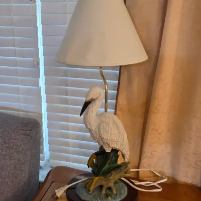 Vintage table lamp featuring a detailed white egret figurine base on a wooden stand, complete with a simple white tapered shade.