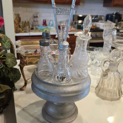 Vintage metal condiment caddy with a tall decorative handle, holding a matching set of glass salt and pepper shakers and cruets.