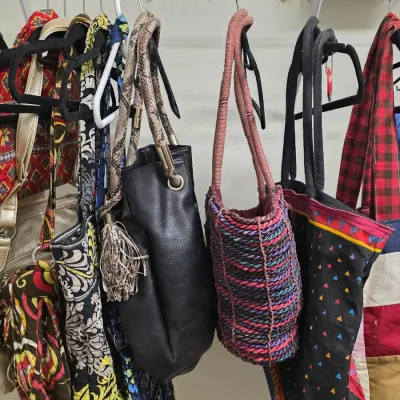 Collection of assorted women's handbags and tote bags, including quilted fabric, faux leather, and woven styles, hanging on a closet...