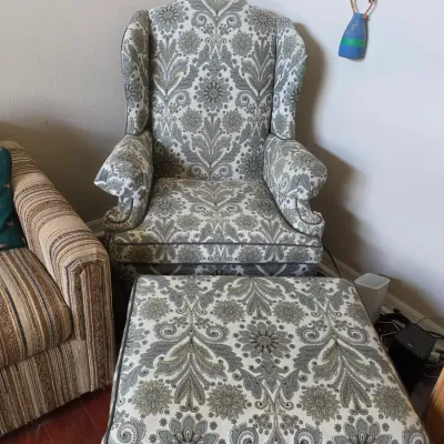 Traditional wingback armchair and matching ottoman upholstered in a grey and white damask floral pattern.