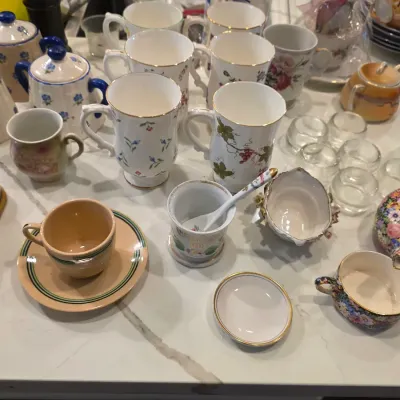 Assortment of vintage porcelain and ceramic tableware, including floral-patterned mugs, teacups with saucers, and small serving dishes.
